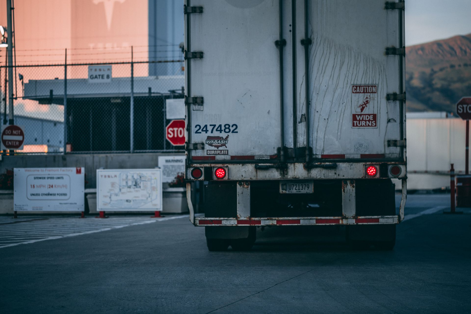 A trailer backed up to a facility gate at dusk, tail lights glowing
