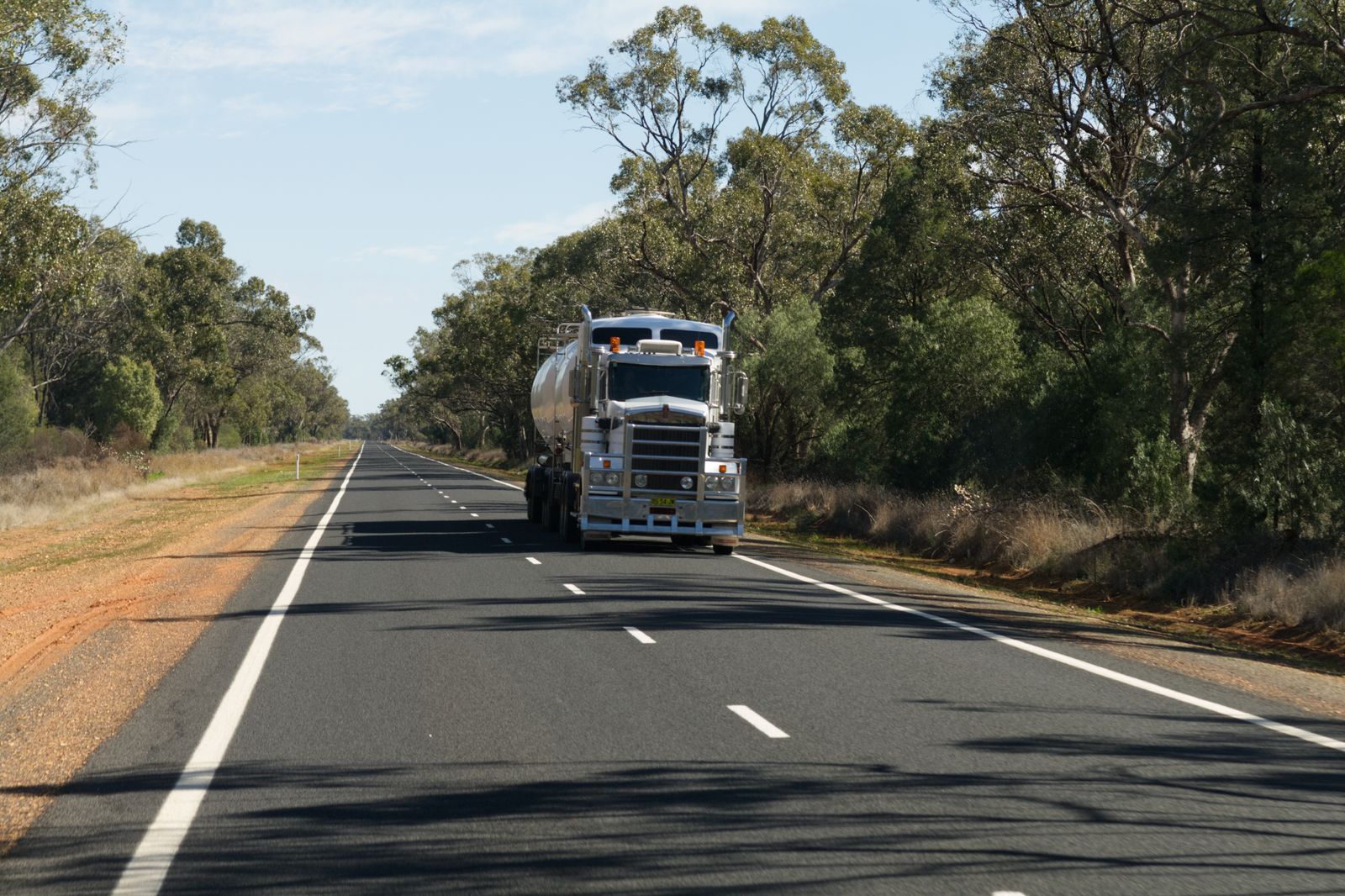 A semi truck rolling down a rural highway lined with trees on a clear day